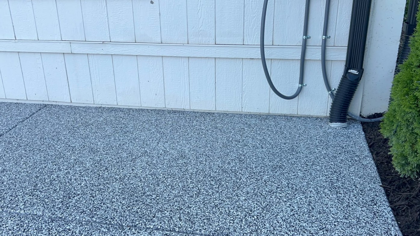 Close-up of patio floor coating meeting white siding, a downspout, and an expansion joint